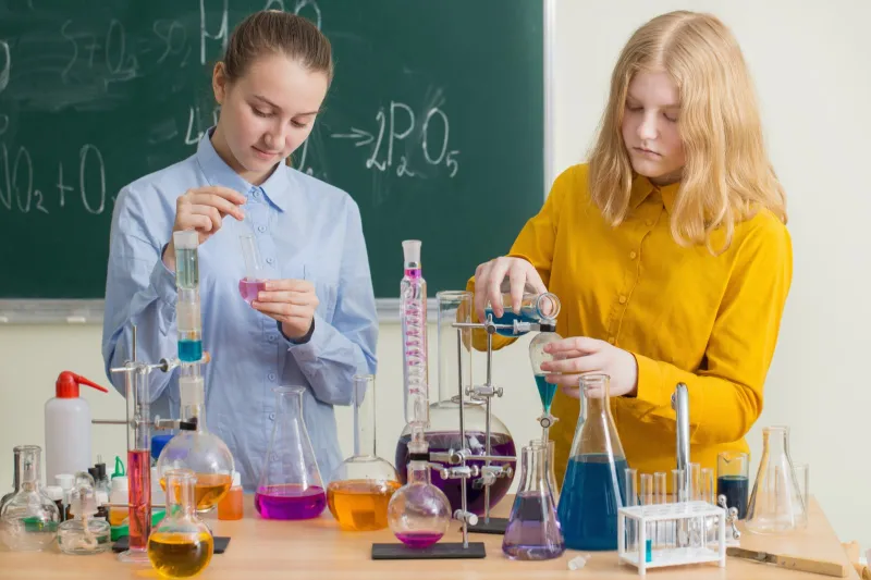 Dwie licealistki przeprowadzają doświadczenia z kolbami i probówkami w szkolnej pracowni chemicznej